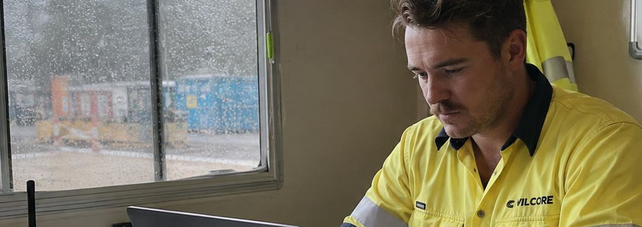 A site supervisor working at a laptop in a site office.